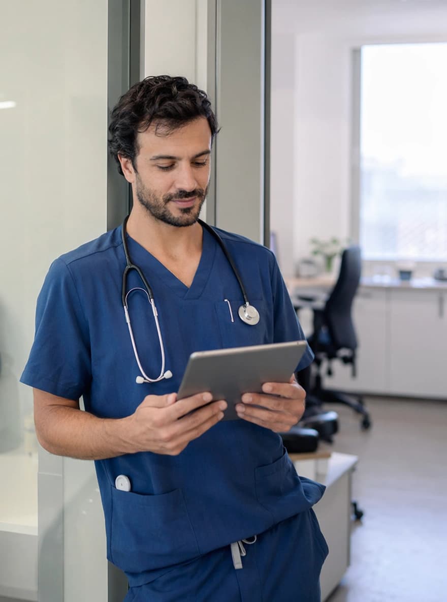 Infermiere che controlla con serenità il calendario turni dal tablet in ambulatorio